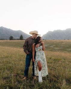 a man and woman standing together in a field with mountains in the backgroud