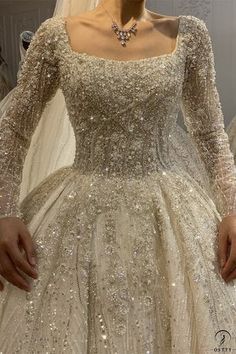 a woman wearing a wedding dress with long sleeves and beading on the skirt is standing in front of mannequins