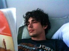 a young man laying in bed next to a pillow with an orange book on it