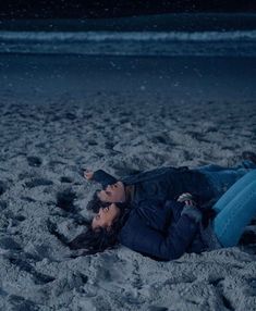 a man and woman laying on the beach in the sand at night with their eyes closed