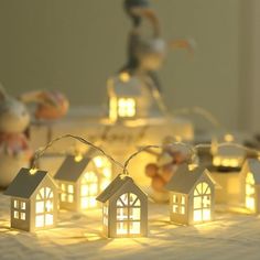 small white houses are lit up with fairy lights on the table next to it is a figurine