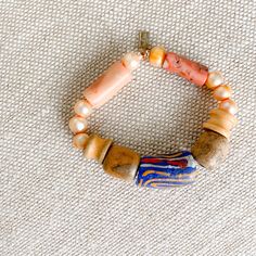 This piece is sustainable. Vibrant blue hue hand painted African prayer bead with light orange, red and white details. Features freshwater pearls in peach, coral, and neutral rose wood from the tree of health and wisdom. Measures 7-8”, regular size. Sterling silver BelleStyle logo tag. Made in USA. One of a kind. Comes in a linen travel pouch. Artisan Orange Bracelet With Colorful Beads, Artisan Orange Bracelets With Colorful Beads, Artisan Orange Hand-strung Beaded Bracelets, Orange Artisan Hand-strung Bracelets, Artisan Orange Hand-strung Bracelets, Orange Wooden Beaded Bracelets As Gift, Orange Wooden Beads Bracelet As Gift, Orange Wooden Beads Bracelet For Gift, Gift Orange Wooden Beaded Bracelets