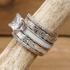 three wedding rings with white gold and diamonds on top of each other in front of a wooden stick