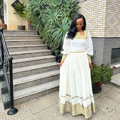 a woman standing in front of some stairs wearing a white and yellow dress with gold trim