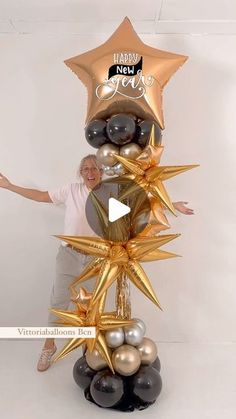 a woman standing next to a tall star shaped balloon with gold and black balloons on it