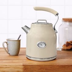 a tea kettle sitting on top of a wooden table next to a mug and cookies