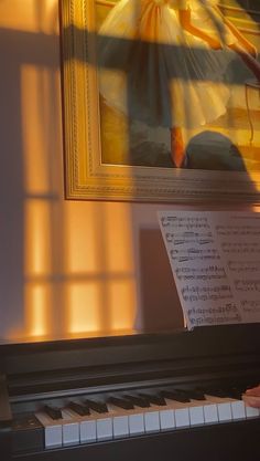 a piano and sheet music are in front of a painting on the wall with sunlight streaming through it