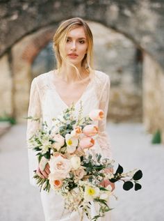 a woman holding a bouquet of flowers in front of an archway with stone walls behind her