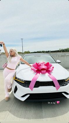 a woman standing next to a white car with a pink bow on it