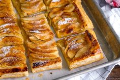 sliced apple tarts sitting on top of a baking sheet covered in powdered sugar