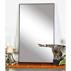 a mirror sitting on top of a wooden shelf next to a candle and glass vase