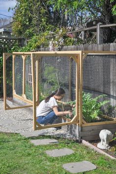 a woman kneeling down in front of a chicken coop with plants growing out of it