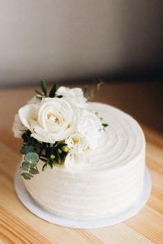 a close up of a cake with white flowers on the top and greenery around it