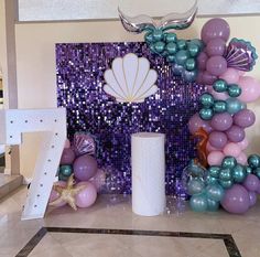 there is a purple and blue balloon arch with mermaid decorations on the wall next to it