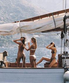 three beautiful women in bikinis sitting on the back of a sailboat and talking