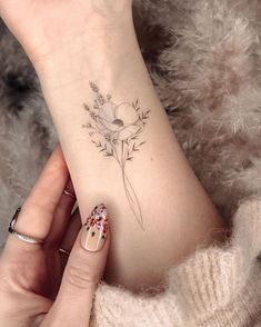 a woman's hand with a flower tattoo on her left wrist and the other arm