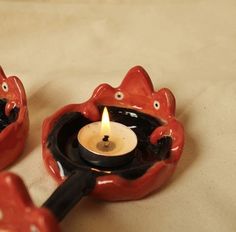 two red ceramic candlesticks sitting on top of a white cloth covered tablecloth