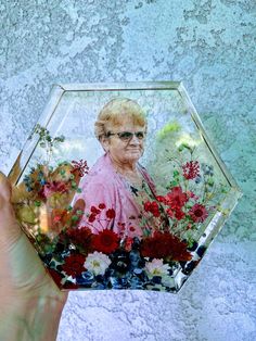 a person holding up a glass photo with flowers in the center and an older woman's face on it