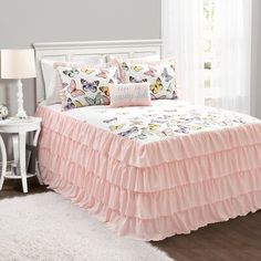 a bed with pink ruffled bedspread and two pillows on top of it