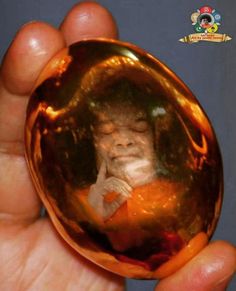 a hand holding an orange glass ball with a buddha image on it's side