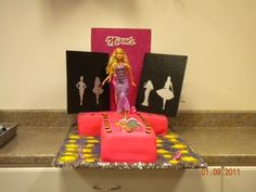 a barbie doll cake on top of a counter with two pictures and a pink purse