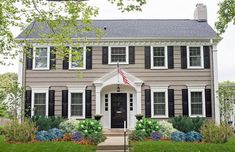 a large gray house with black shutters and white trim on the front door is shown