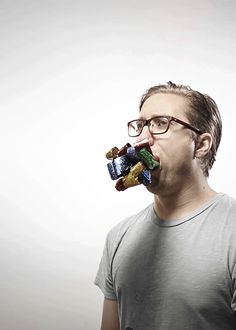 a man with glasses is eating something out of his mouth while standing in front of a white background