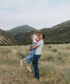 a man holding a woman in the middle of a field with mountains in the background