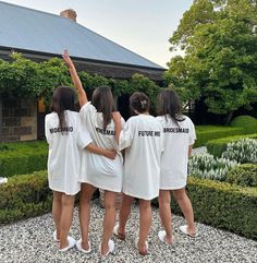 three girls in white shirts are standing together and pointing to the sky with their hands