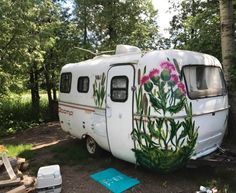 an old camper with flowers painted on the side is parked in front of some trees