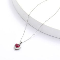 This rhodium over sterling silver pendant features a 7x7 mm heart shaped lab created ruby in the center accented with 28 pieces of round cut moissanite stones of 1.4 mm around the main stone creating a halo necklace design. Heart Cut Cubic Zirconia Birthstone Necklace, Cubic Zirconia Heart Necklace With Gemstone For Valentine's Day, Heart Necklace With Cubic Zirconia For Valentine's Day, Valentine's Day Heart Necklace With Cubic Zirconia Gemstone, Cubic Zirconia Heart Necklace With Gemstone, Red Cubic Zirconia Heart Pendant Necklace, Red Heart-shaped Cubic Zirconia Necklace, Cubic Zirconia Gemstone Heart Pendant Necklace, White Gold Heart Cut Gemstone Necklace