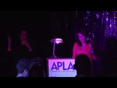 a woman standing in front of a microphone on top of a sign that says apla