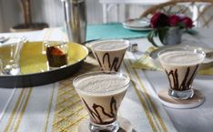 two glasses filled with liquid sitting on top of a table next to plates and silverware