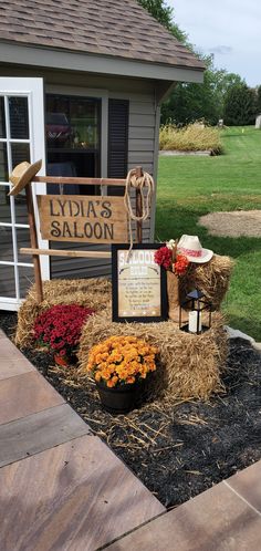 a sign that is sitting in the grass near some flowers and hay with a cowboy hat on it