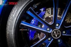 the front wheel of a blue sports car with chrome spokes and black rims