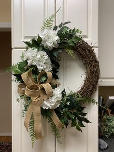 a wreath with white flowers and greenery hangs on a door