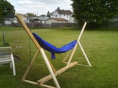 a blue hammock sitting on top of a wooden stand in the grass next to a bench