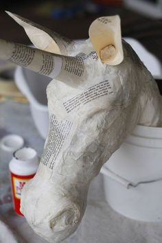 an animal head made out of newspaper sitting on top of a table next to paint cans