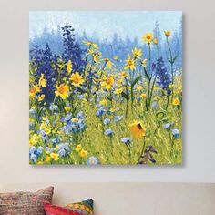 a painting of yellow and blue flowers on a white wall above a bed with pillows