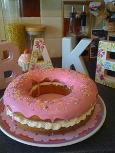 a pink frosted donut sitting on top of a plate next to the letter k