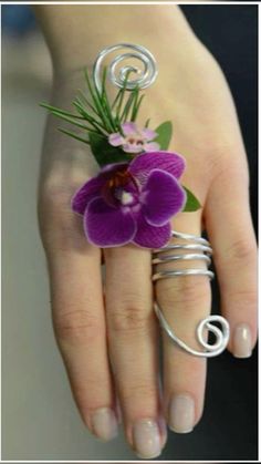 a woman's hand holding a purple flower and wire ring with green leaves on it