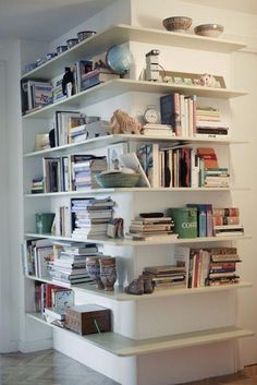 a book shelf filled with lots of books on top of a hard wood floor next to a white wall