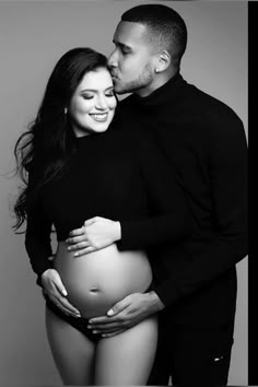 a pregnant couple cuddles and kisses while posing for a black and white photo