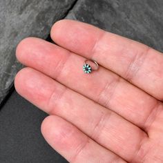 a person's hand holding a tiny ring with a turquoise flower on it,