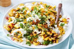 a white plate topped with corn salad and sour cream dressing next to a wooden spoon