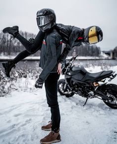 a man in black jacket and helmet holding onto another person's leg while standing next to a motorcycle