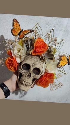 a human skull with flowers and butterflies on it's head is being held by someone