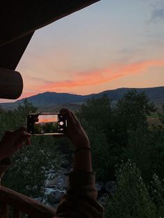 a person taking a photo with their cell phone at the top of a balcony overlooking a river and mountains