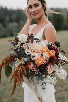 a woman in a white dress holding a large bouquet with orange and pink flowers on it