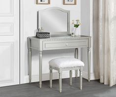 a white dressing table with a mirror and stool next to a potted plant on a rug